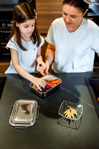 Mother and child packing lunch into a stainless-steel box.
